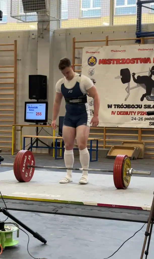 Mężczyzna w sportowym stronu, przed nim leży sztanga.