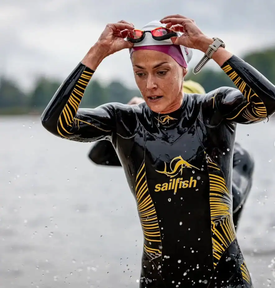 Triathlonistka w stroju sportowym z logo Sailfish, przygotowująca się do pływania w jeziorze.