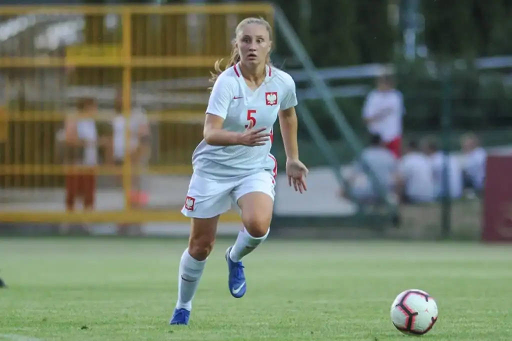 Piłkarka w akcji podczas meczu, grająca w reprezentacji Polski, na boisku sportowym.
